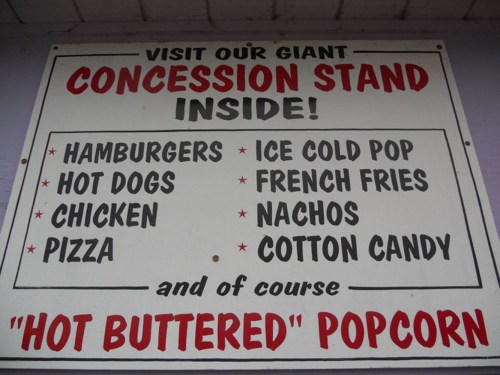 Sign advertising a concession stand with items like hamburgers, hot dogs, chicken, pizza, and popcorn.