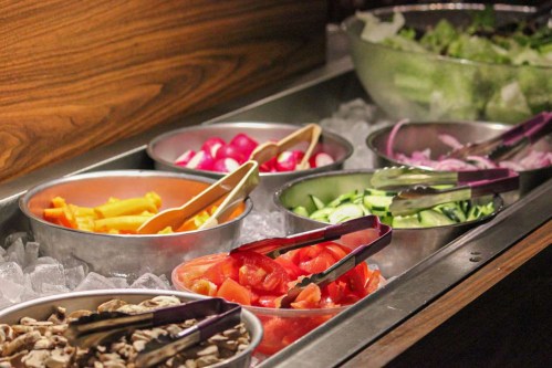 A variety of fresh vegetables in bowls on ice, including tomatoes, cucumbers, radishes, and lettuce.