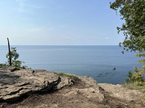 A serene view of a calm lake from a rocky cliff, with a small boat in the distance under a clear blue sky.