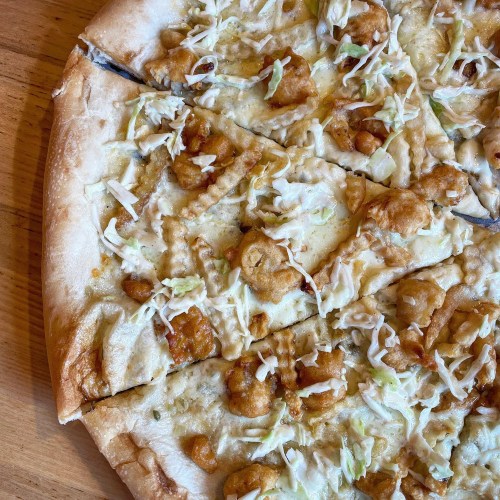 A close-up of a pizza topped with fried chicken, shredded cabbage, and a creamy sauce, sliced into pieces.