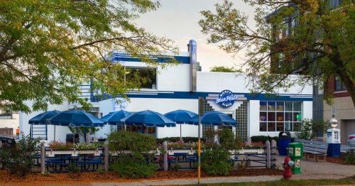 A retro-style diner with blue umbrellas and outdoor seating, surrounded by trees and autumn leaves.
