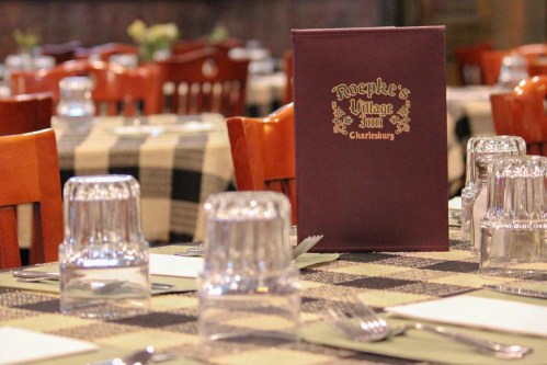 A dining table set with checkered tablecloths, glassware, and a menu for Roepke's Village Inn.
