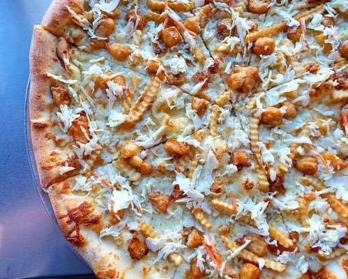 A close-up of a pizza topped with shredded cabbage, crispy chicken pieces, and a golden crust.
