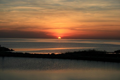 A serene sunset over calm waters, with vibrant orange and yellow hues reflecting on the surface.