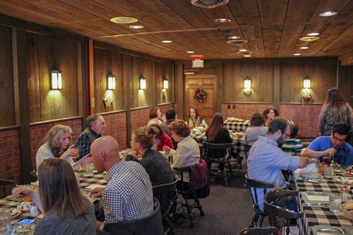 A cozy restaurant interior with diners at tables, wooden walls, and warm lighting, creating a welcoming atmosphere.