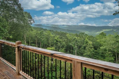 Scenic view from a wooden deck overlooking lush green mountains and a cloudy blue sky.