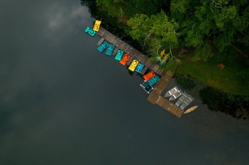 Aerial view of a dock with colorful paddle boats on a calm lake surrounded by greenery.