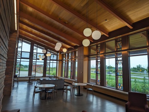 Bright, modern interior of a café with large windows, wooden beams, and stylish furniture.