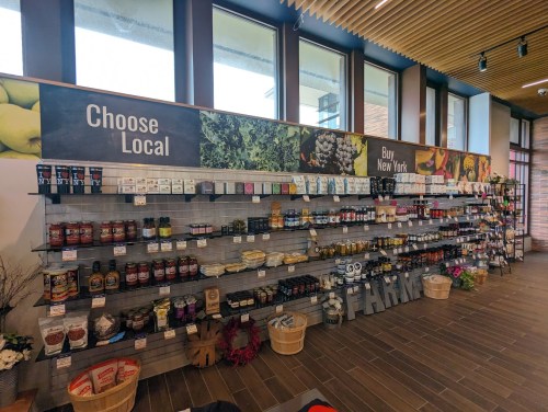 A grocery store display featuring local products, with shelves of jars, boxes, and baskets under a "Choose Local" sign.