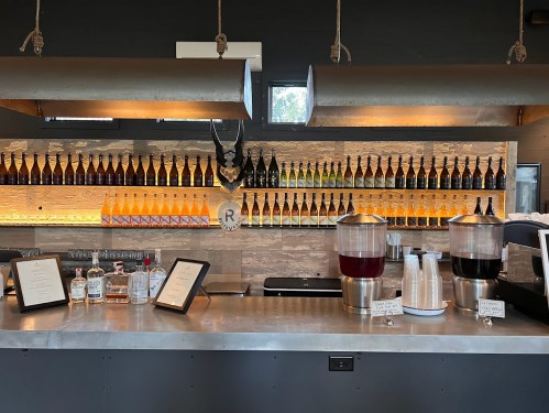 A modern bar with a variety of bottles on shelves, featuring drink dispensers and a sleek countertop.