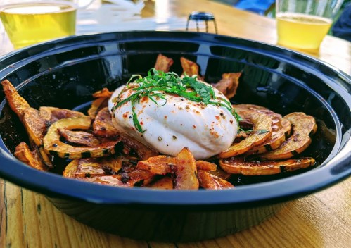 A black bowl filled with roasted squash slices topped with a creamy burrata and garnished with herbs.