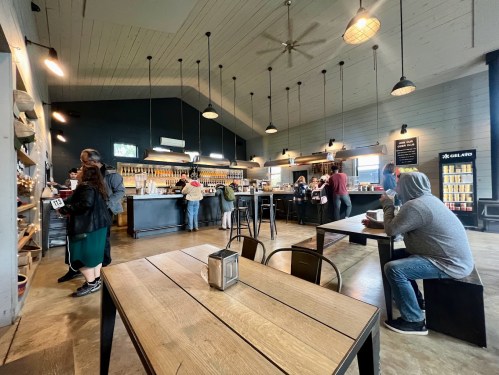 A cozy café interior with customers at the counter and tables, featuring wooden decor and a bright atmosphere.