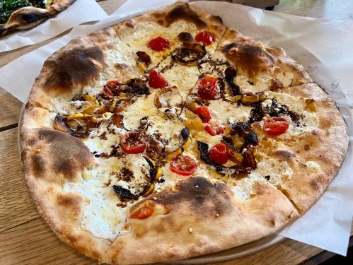 A freshly baked pizza topped with cherry tomatoes, caramelized onions, and a golden crust, served on parchment paper.
