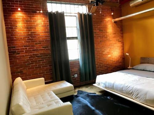 Cozy room with exposed brick walls, a bed, a white sofa, and large windows with dark curtains.