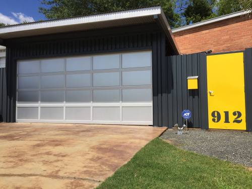 A modern garage with a large glass door, yellow side door, and a bright yellow house number 912 on the wall.
