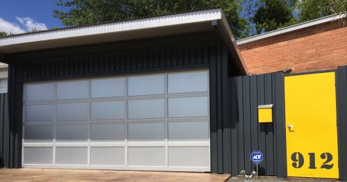 A modern garage with a gray door and a bright yellow side door, featuring the number 912 on the wall.