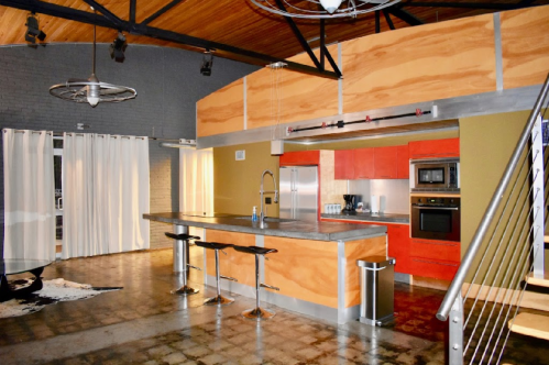 Modern kitchen with red cabinets, stainless steel appliances, and a large island with bar stools under a wooden ceiling.