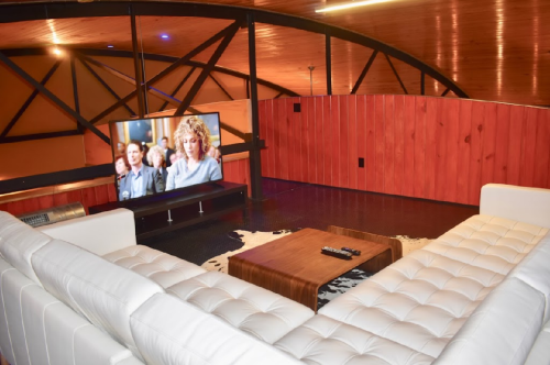 Cozy living room with a white sectional sofa, wooden coffee table, and a large TV displaying a scene from a show.