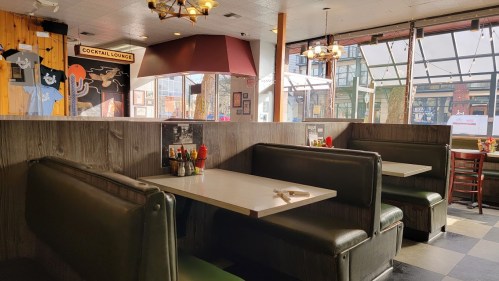 Interior of a diner with empty booths, a cocktail lounge sign, and large windows letting in natural light.