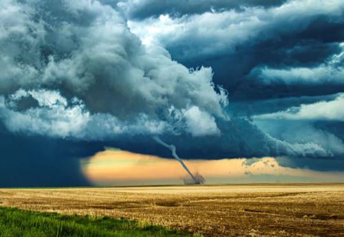 A dramatic sky with dark storm clouds and a visible tornado forming over a flat, golden field at sunset.