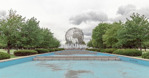 A globe sculpture surrounded by trees and a water feature, set against a cloudy sky.