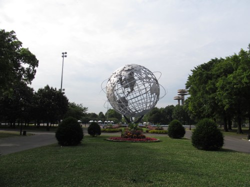 A large metallic globe sculpture surrounded by greenery and flowers in a park setting.