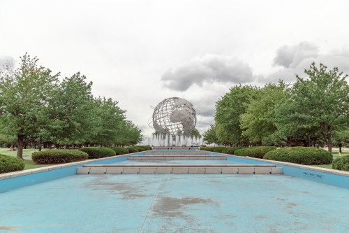 A large globe sculpture surrounded by greenery and a blue walkway under a cloudy sky.