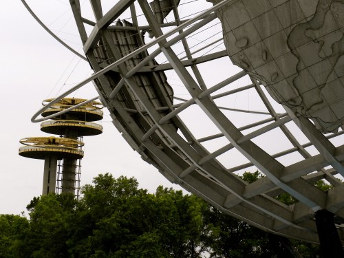 A close-up of a metallic globe sculpture with a tower in the background, surrounded by trees under a cloudy sky.
