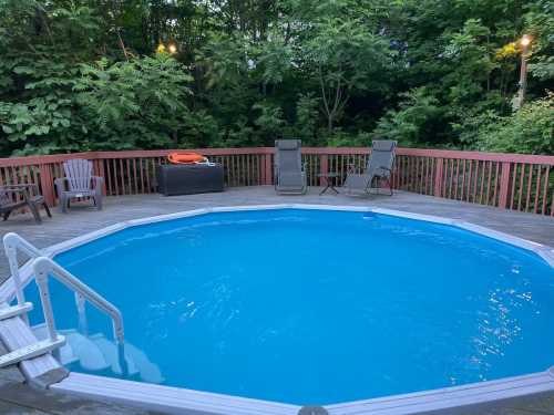 A serene backyard with an oval pool, wooden deck, and lounge chairs surrounded by lush greenery.