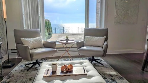 Cozy living room with two chairs, a small table, and a view of the ocean through large windows.