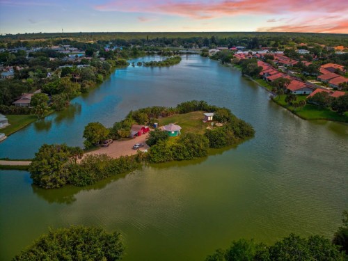 Aerial view of a serene island surrounded by water, with lush greenery and a few buildings along the shoreline.