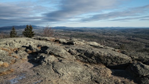 A rocky landscape with distant hills and a cloudy sky, showcasing a panoramic view of the serene countryside.