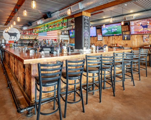 A rustic bar with wooden decor, high stools, and multiple TVs displaying sports, set in a lively atmosphere.