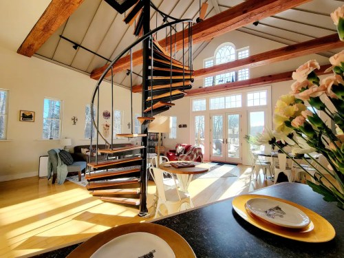 Bright, modern interior featuring a spiral staircase, wooden beams, and cozy seating areas with large windows.