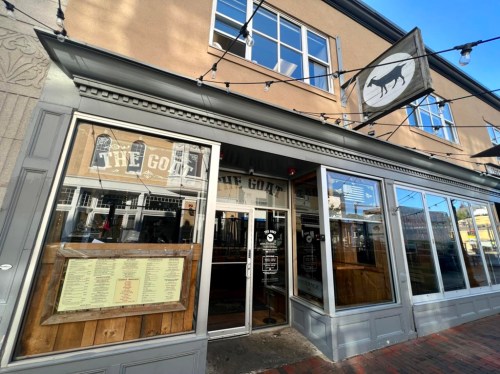 Exterior of a restaurant named "The Goat," featuring large windows and a wooden menu display.