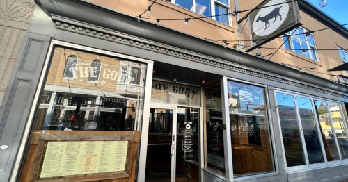 Exterior of a restaurant called "The Goat," featuring large windows and a menu displayed outside.