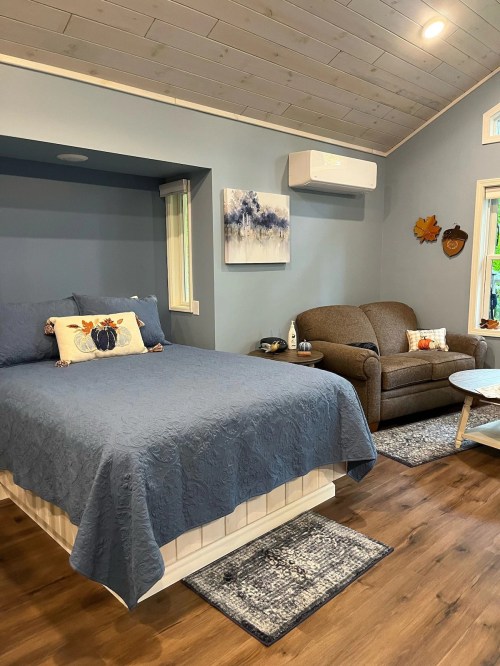 Cozy room featuring a bed with blue bedding, a sofa, and light blue walls, accented by artwork and decorative items.