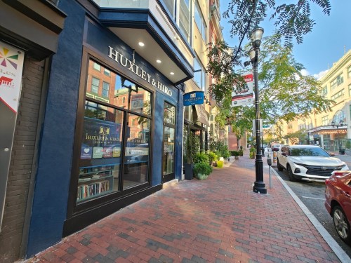 A storefront labeled "Huxley & Hiro" on a brick sidewalk, with trees and buildings in the background.