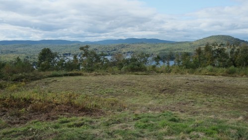 A scenic view of rolling hills and a lake, surrounded by lush greenery under a partly cloudy sky.