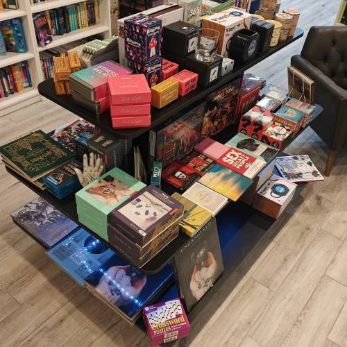 A display table filled with various books, games, and colorful boxes in a cozy bookstore setting.