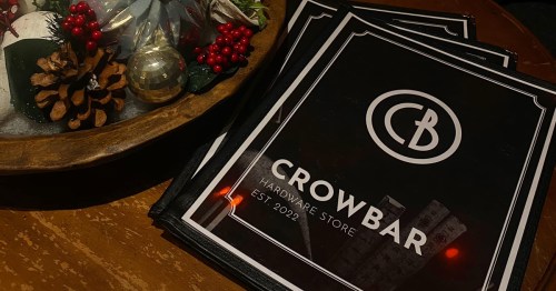 A stack of menus for "Crowbar Hardware Store," established in 2022, next to a festive holiday centerpiece.
