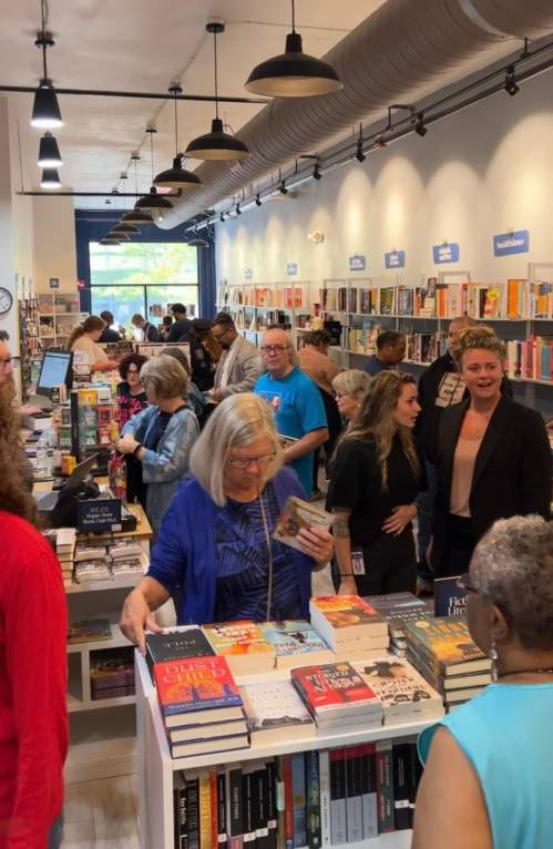 A busy bookstore filled with people browsing books and engaging in conversation. Shelves lined with various titles.