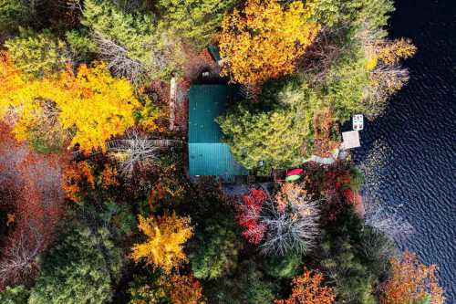 Aerial view of a cabin surrounded by vibrant autumn foliage and a calm lake.