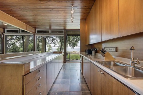 Modern kitchen with wooden cabinets, stainless steel sink, and large windows overlooking a scenic outdoor view.