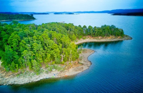 Aerial view of a lush green island surrounded by calm blue waters and distant hills under a cloudy sky.