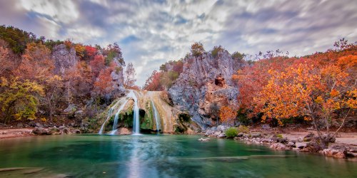 A serene waterfall cascades into a tranquil pool, surrounded by vibrant autumn foliage and rocky cliffs.
