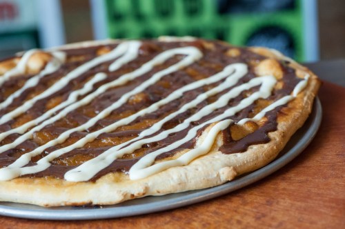 A close-up of a dessert pizza topped with chocolate and white icing drizzles on a wooden surface.