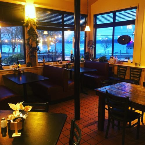 Cozy restaurant interior with booths, tables, and large windows showing a view of the water at dusk.