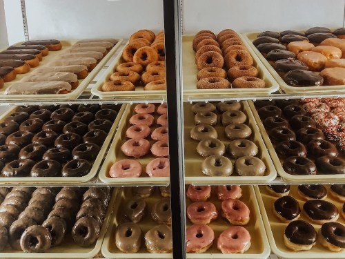 A display case filled with various types of donuts, including glazed, chocolate, and sprinkles, arranged on trays.