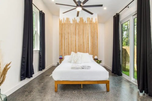 Bright bedroom with a wooden accent wall, large windows, and a cozy bed, featuring modern decor and natural light.
